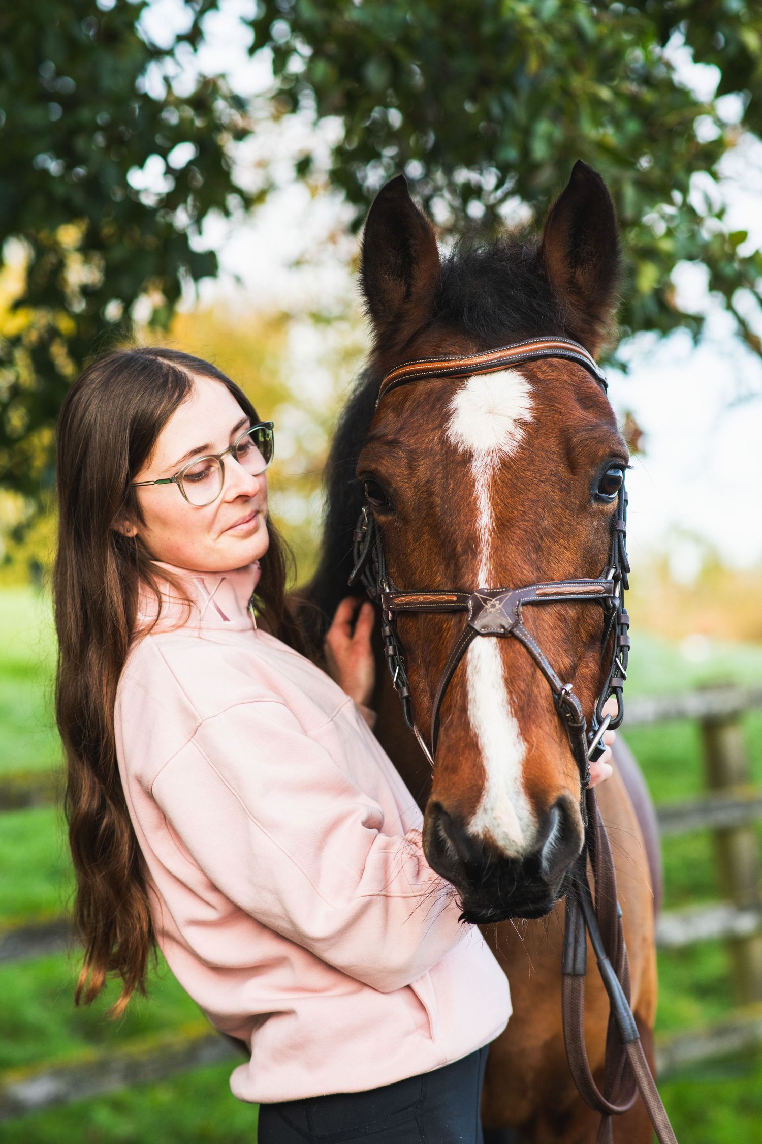 A close-up portrait of a bay horse with its handler against a green background.