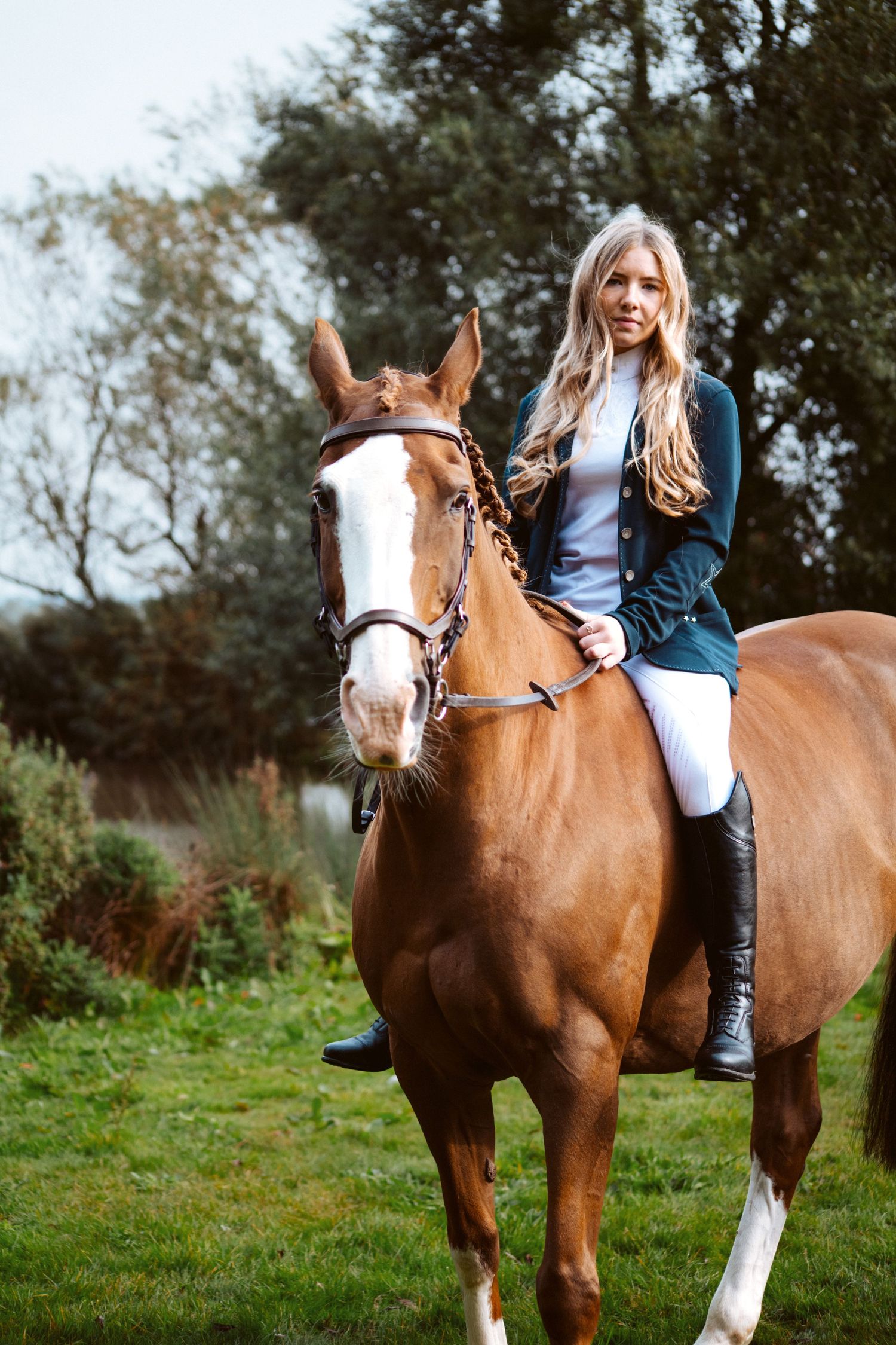 A rider on a chestnut horse with white markings wearing equestrian attire in a green field.
