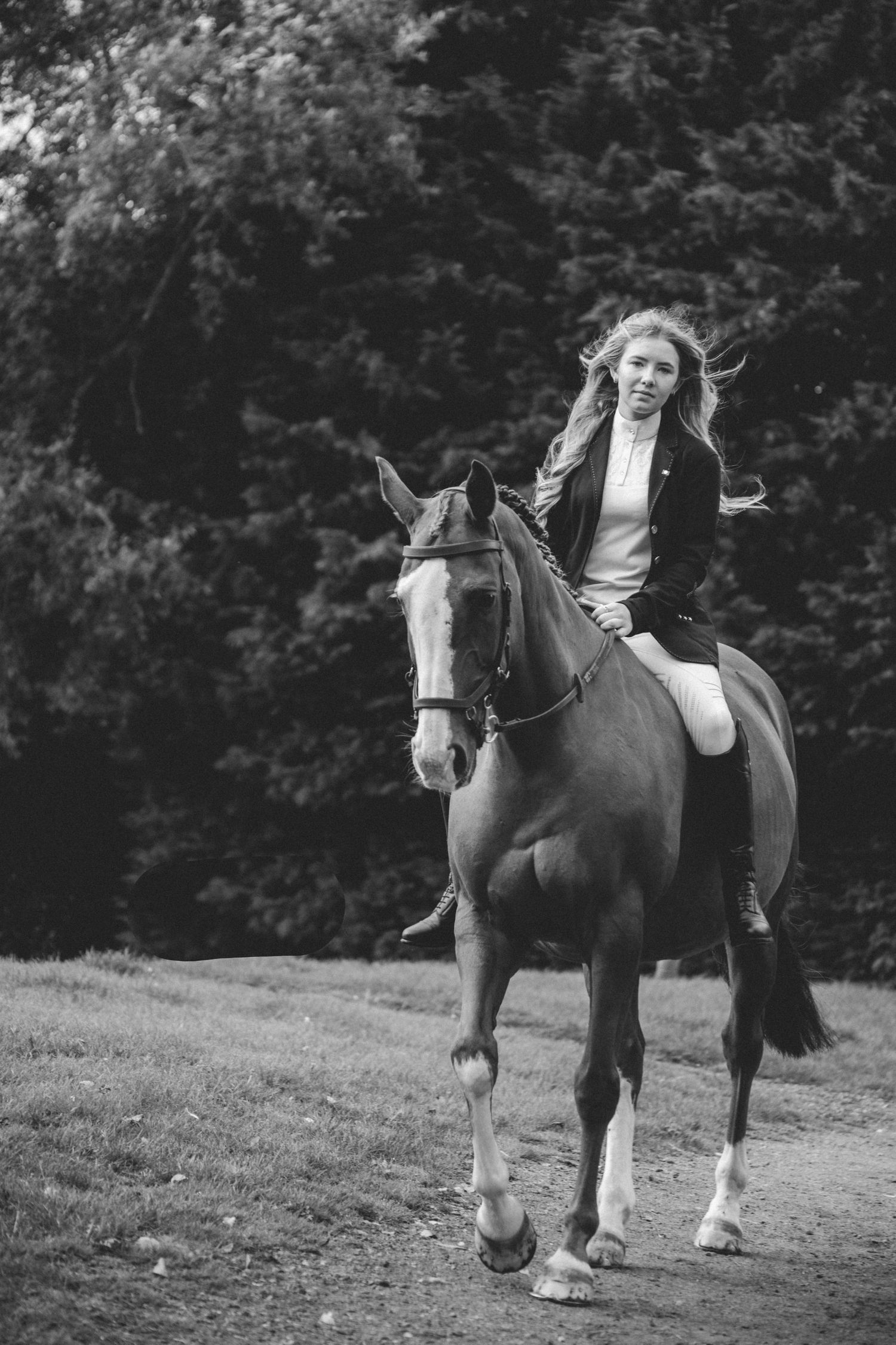 A black and white photo of horseback riding through a wooded area.