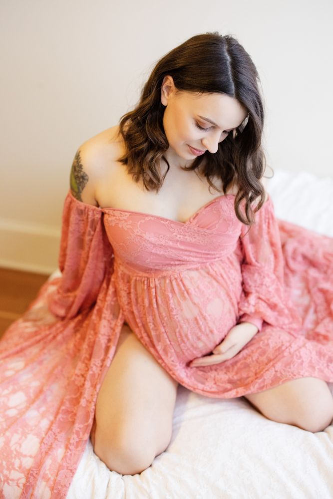 pregnant woman kneeling on a bed in a pink lace dress
