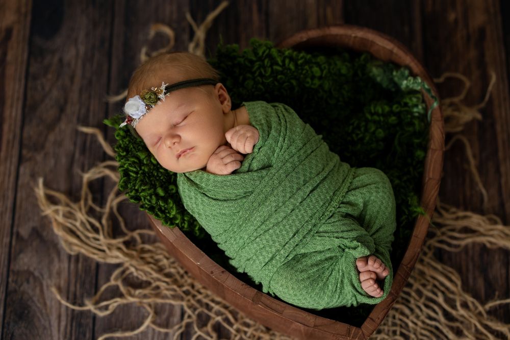 a newborn swaddled in a green cloth placed in a heart shaped wooden crate