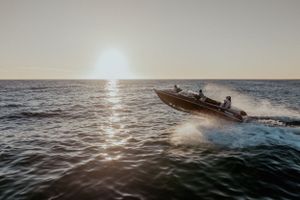 Speed boat jumping waves during sunset over ocean horizon.