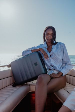 Person in striped shirt sitting with gray luggage on boat seat.