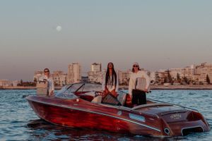 Red vintage boat with passengers against urban skyline at dusk.