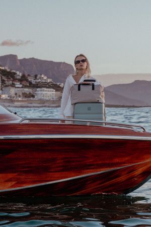 Sleek red wooden boat cruising near mountainous coastline at sunset.