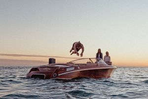 A person performs a backflip off a speedboat during sunset on calm waters.