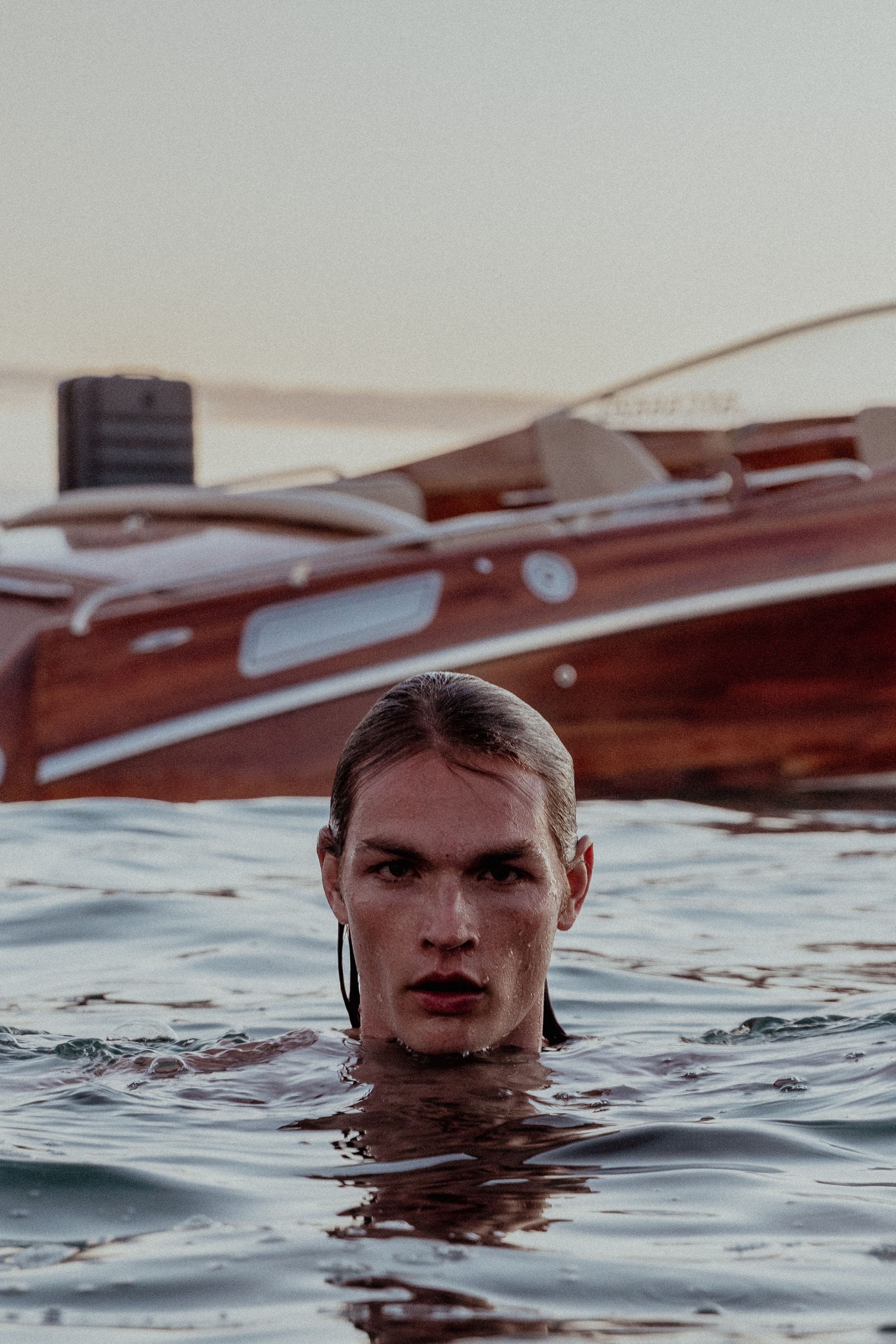 Person swimming in ocean water next to wooden boat at dusk.