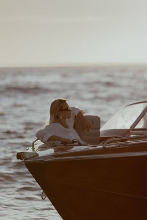 A silhouetted figure relaxes on the bow of a boat against a hazy ocean backdrop at dusk.