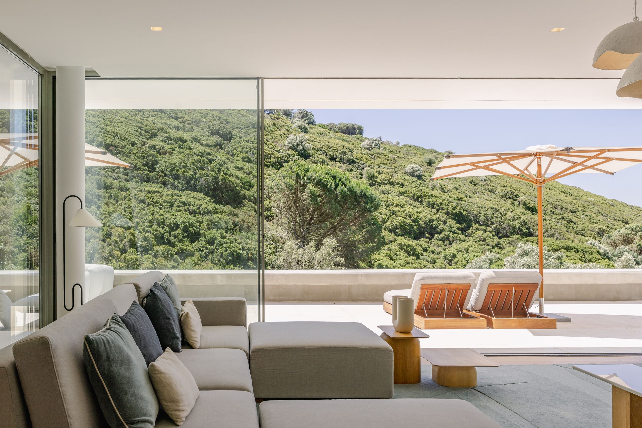 Modern living room with panoramic views of lush hillside and outdoor deck seating.