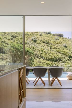 Contemporary dining area with modern chairs overlooking green coastal landscape through large windows.