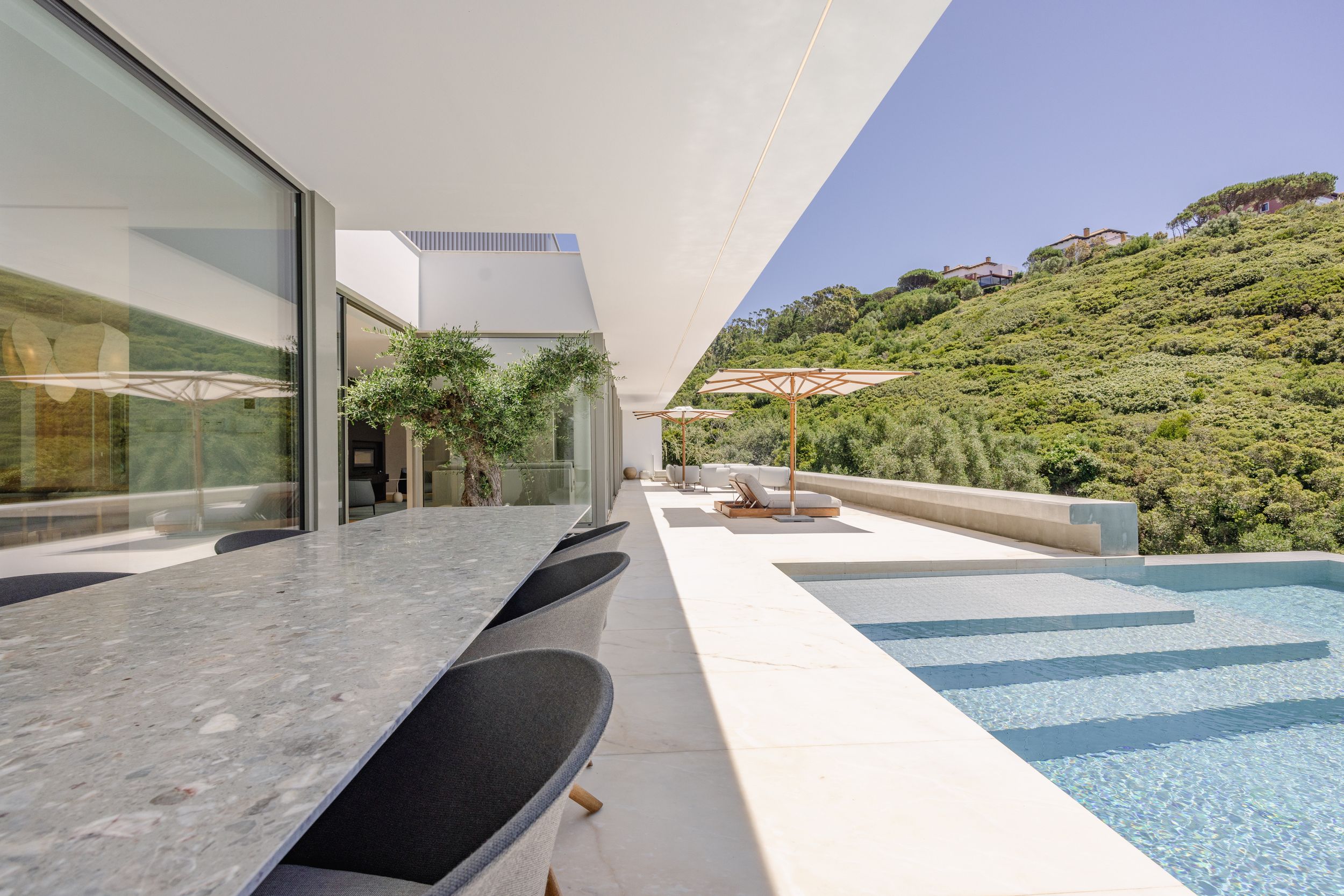 Modern luxury villa terrace with infinity pool and mountain views showcasing sleek outdoor furniture and glass walls.