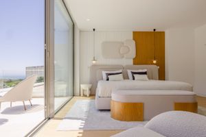 Contemporary bedroom with floor-to-ceiling windows, white bedding, and wooden accents overlooking a scenic view.