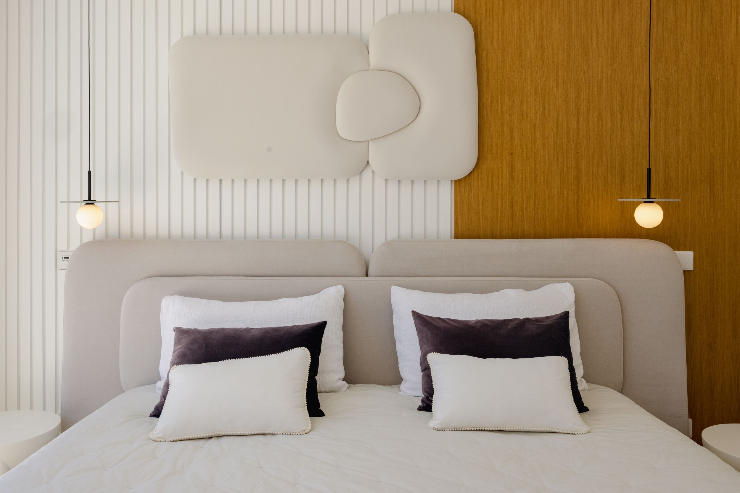 Minimalist bedroom interior featuring white bedding, wooden panels, and modern pendant lighting.