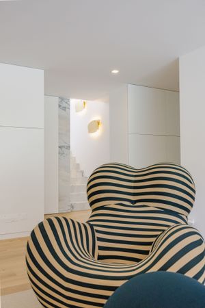 Unique striped lounge chair in black and white pattern positioned in a minimalist white interior.
