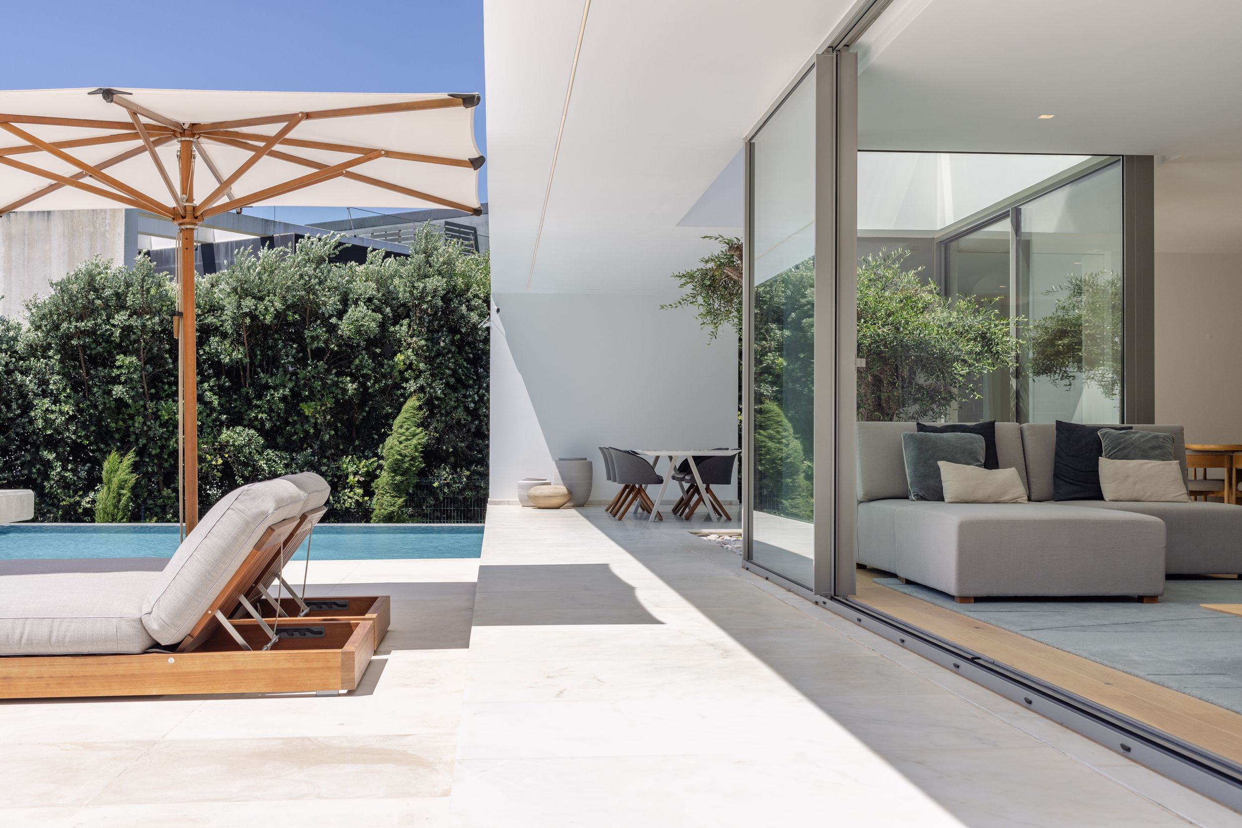 Luxurious poolside terrace with wooden sun loungers and contemporary sliding glass doors.