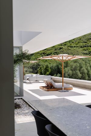 Modern patio space with wooden umbrella and loungers overlooking lush hillside vegetation.