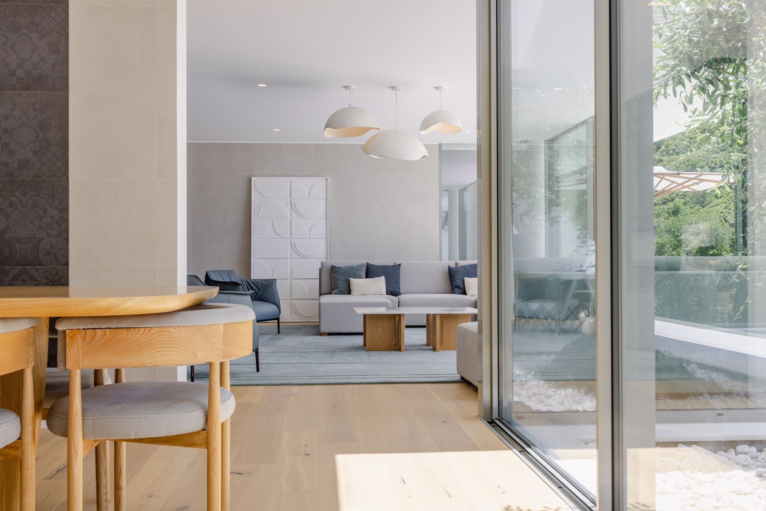 Bright open-plan interior with wooden dining furniture and floor-to-ceiling windows.