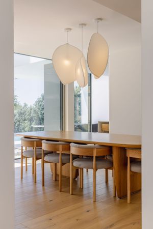 Elegant dining room with oval pendant lights and wooden table setting overlooking outdoor views.