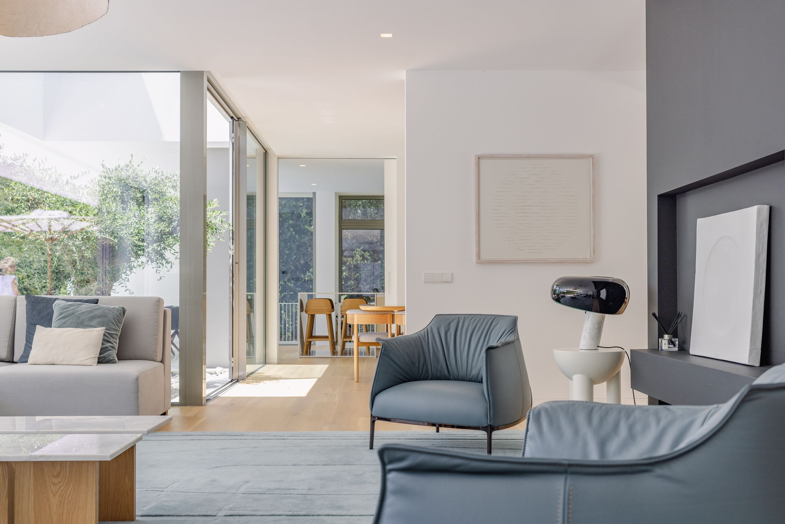 Minimalist living room with gray armchairs and floor-to-ceiling windows offering bright natural lighting.