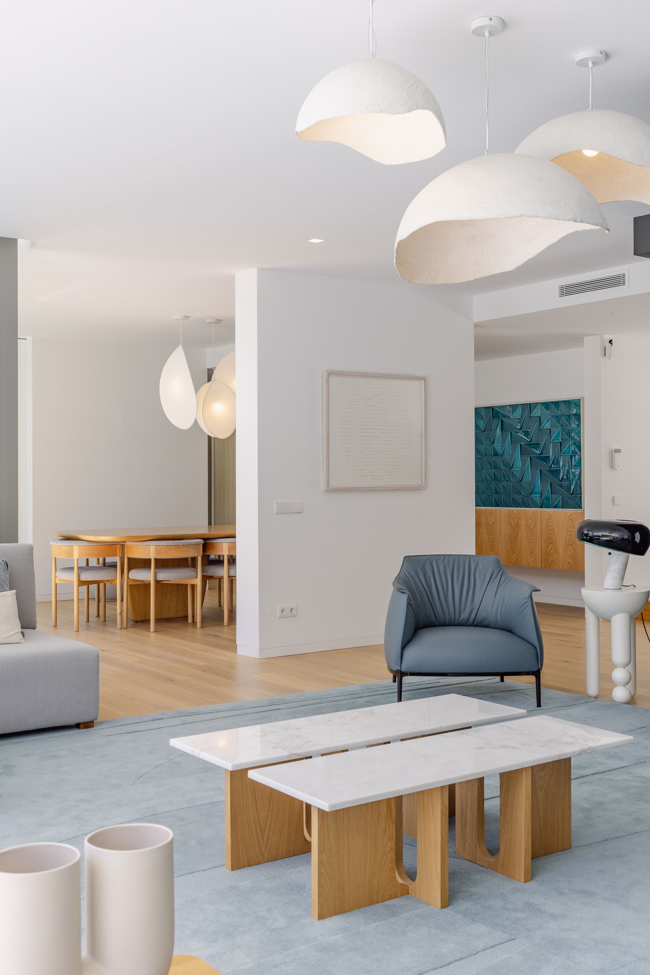 Modern open-plan living space with sculptural pendant lights and wooden accent furniture.
