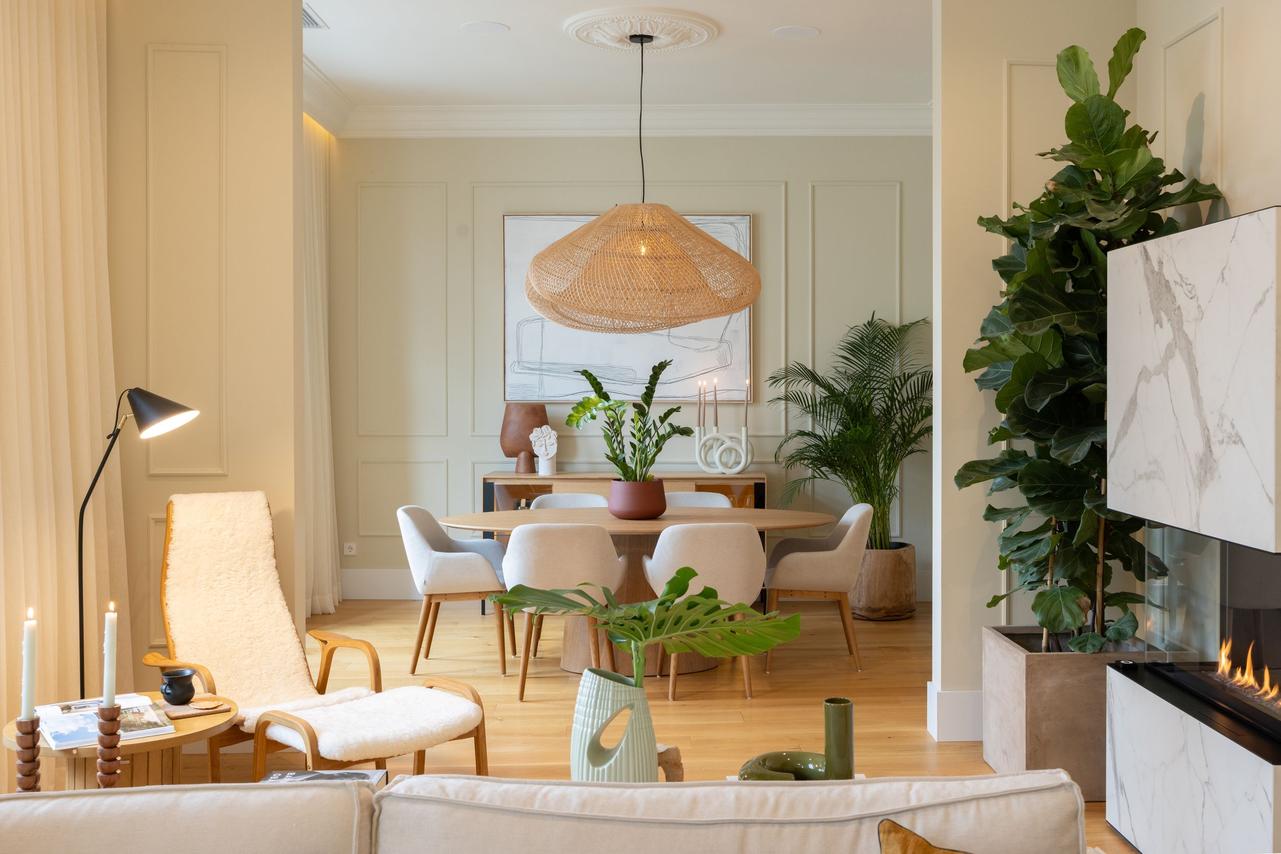Modern dining room with woven pendant lamp, white chairs, and lush plants.