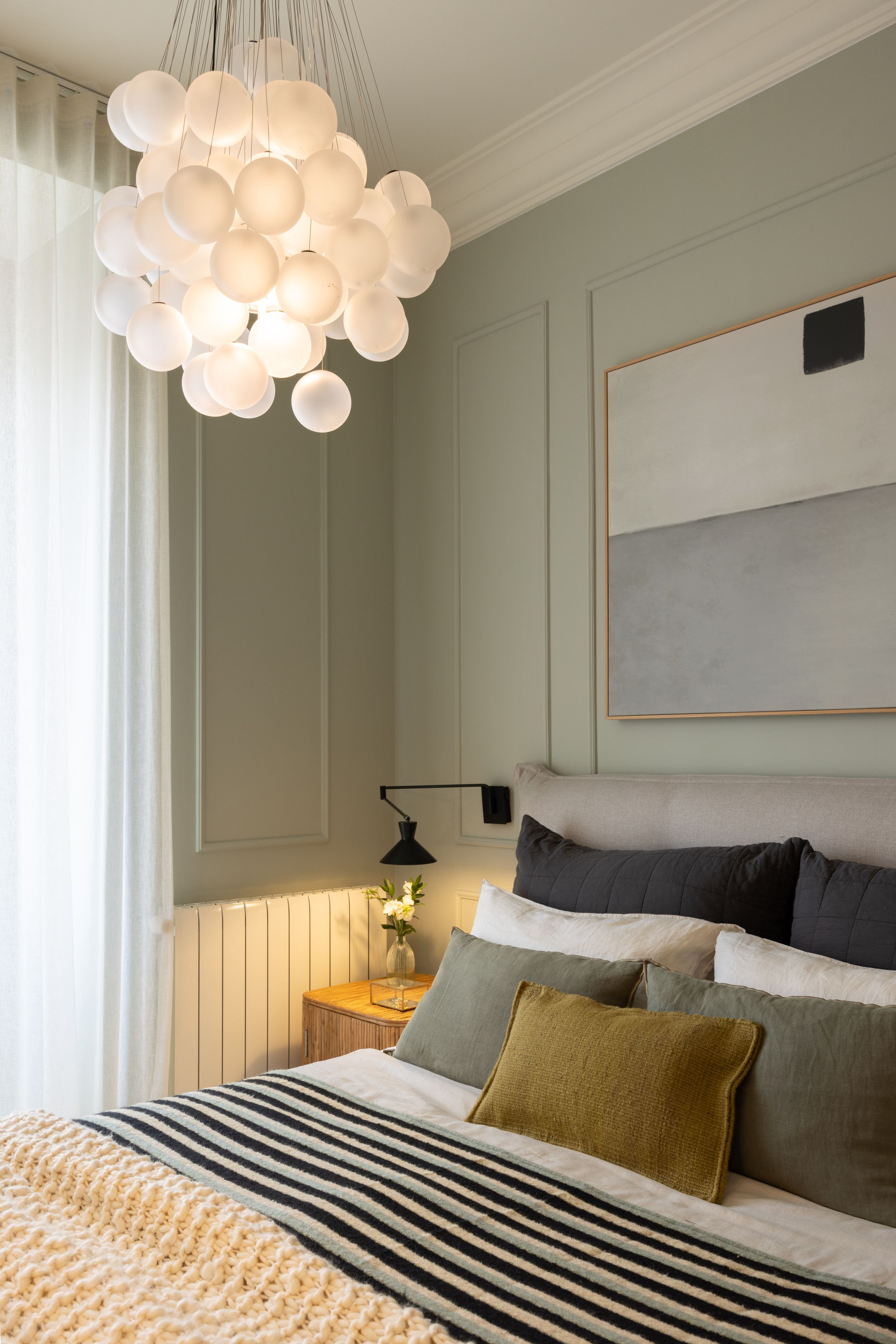 Elegant bedroom with bubble chandelier, textured bedding, and minimal wall art.