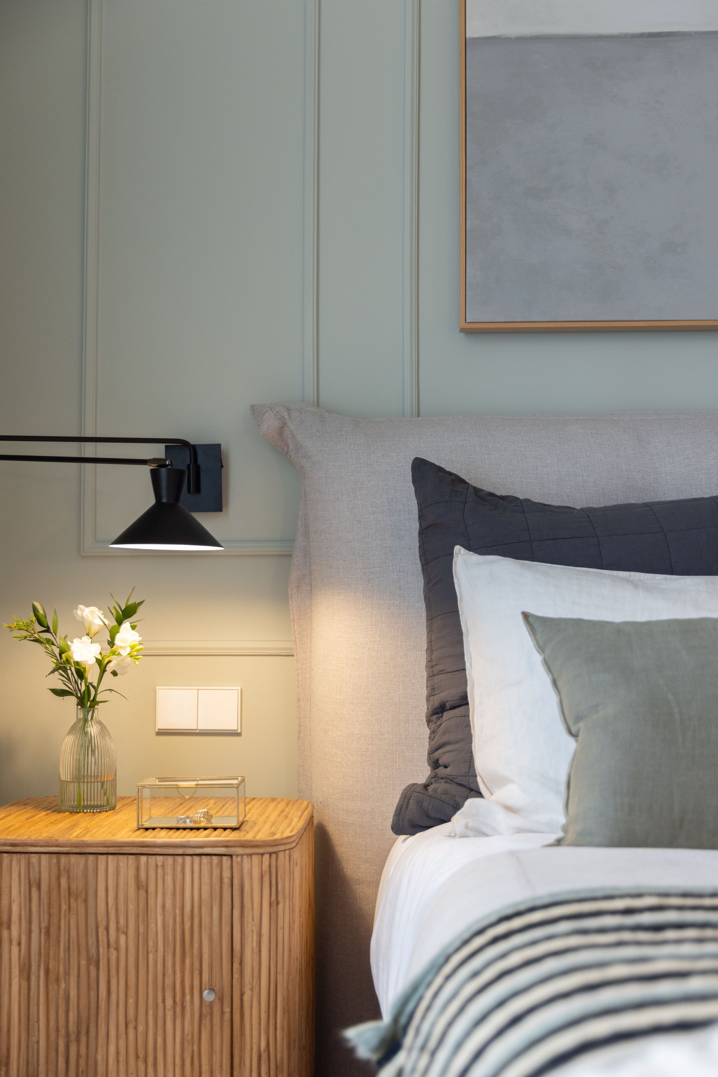 Contemporary bedside table styling with wall sconce, fresh flowers and layered bedding.