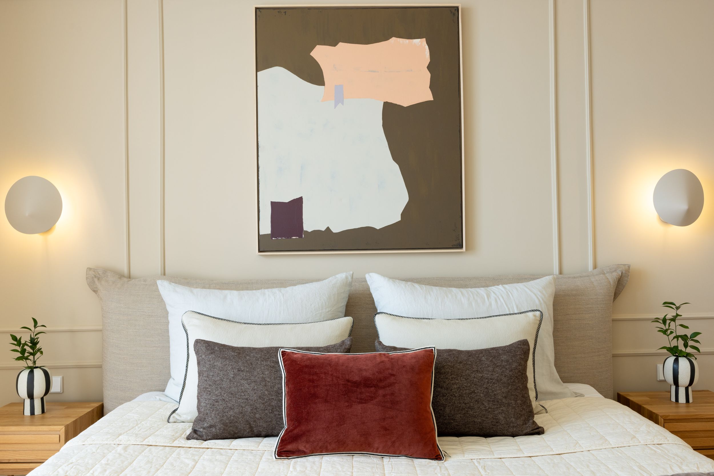 Modern bedroom featuring abstract wall art, circular sconces, and burgundy accent pillows.