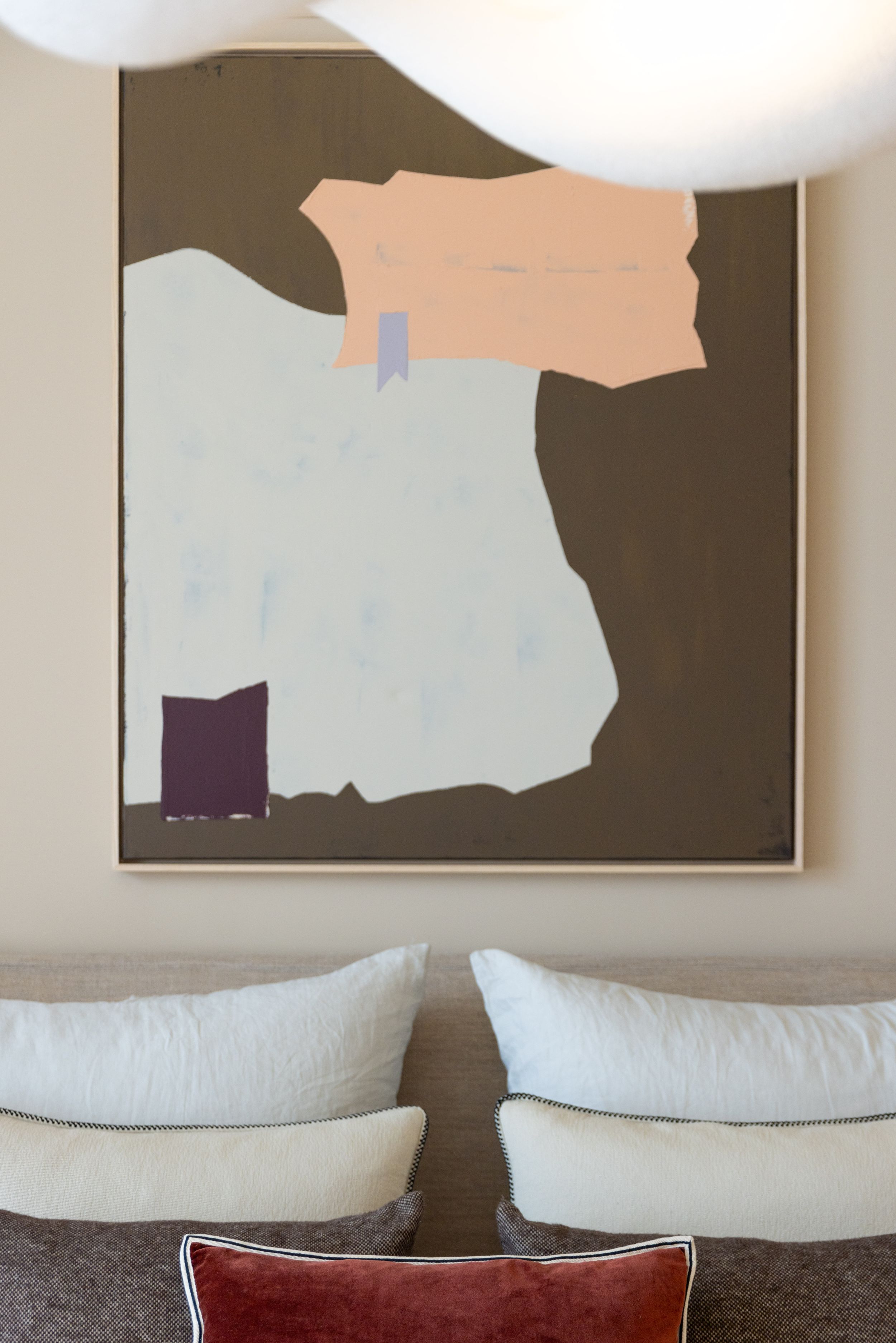 Abstract geometric artwork in neutral tones hanging above plush cushions and pillows.