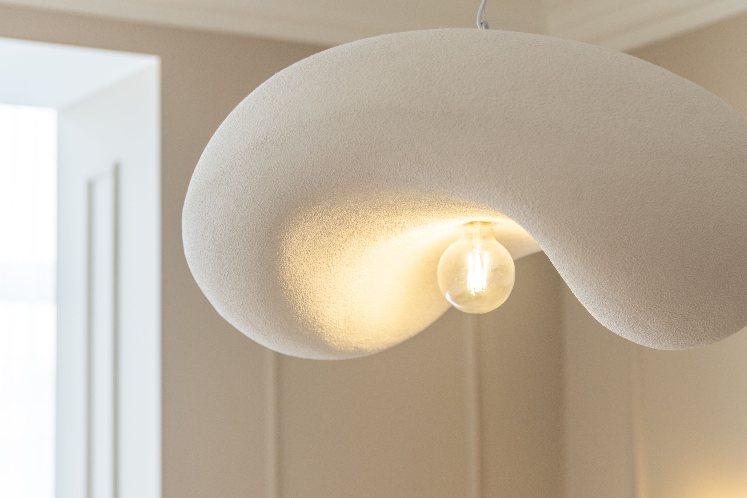 Close-up of curved white pendant light fixture glowing warmly against ceiling.