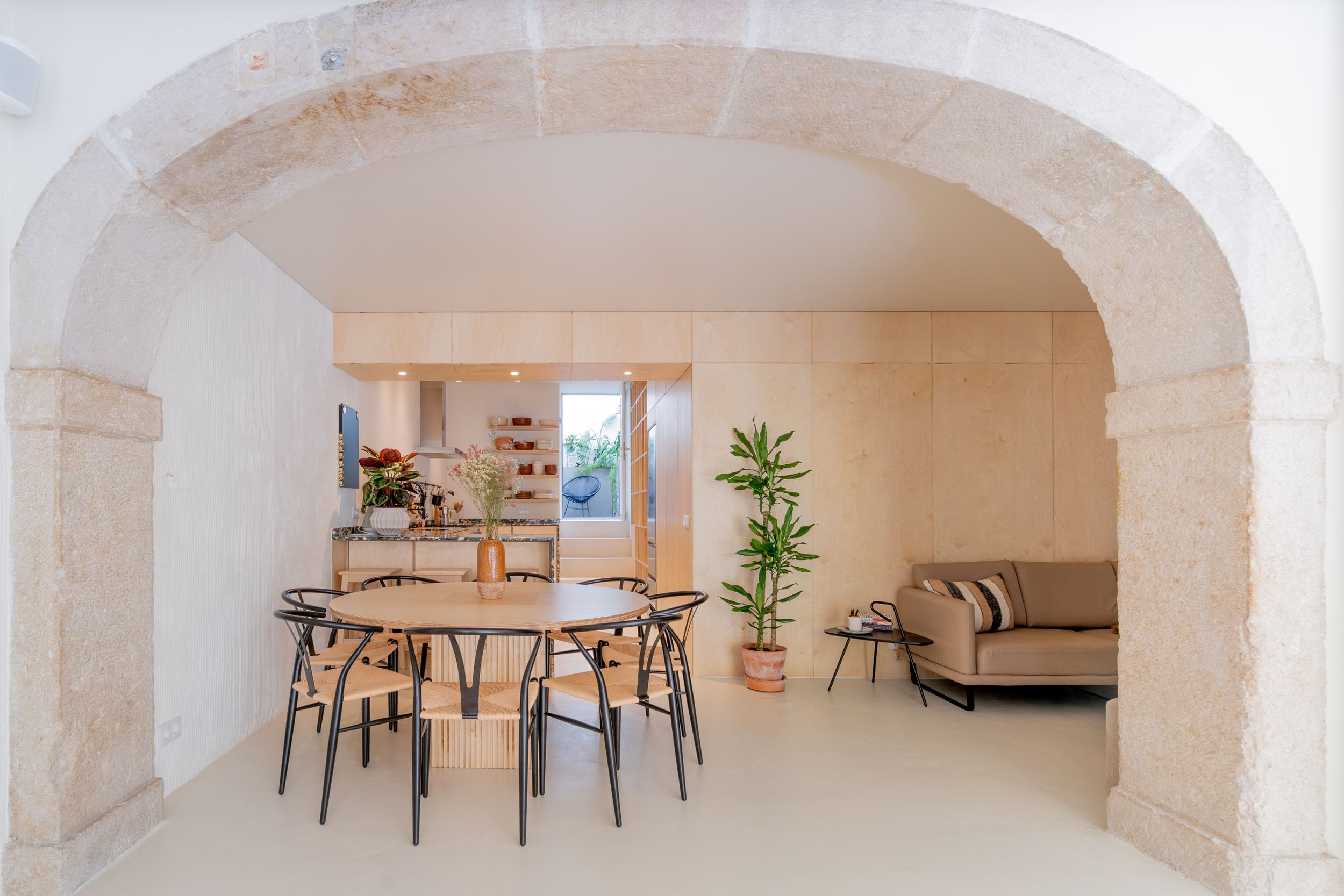 Open concept dining and living area with stone arch and modern furniture in neutral tones.