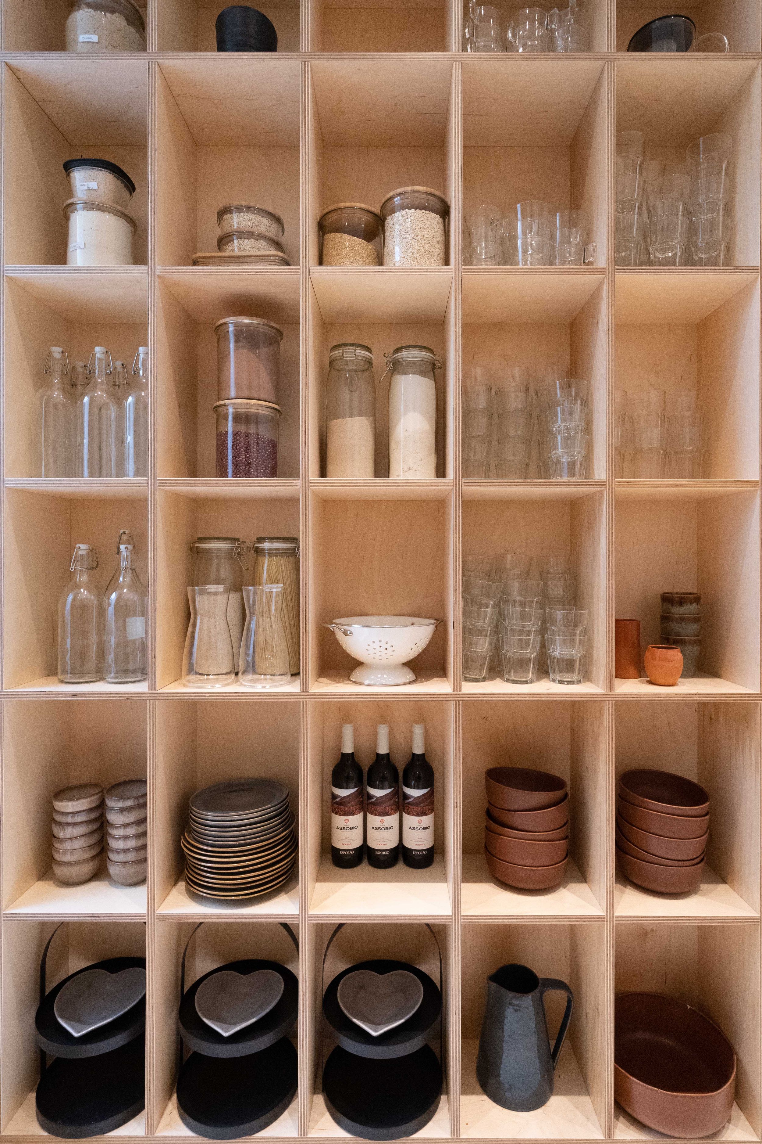 Organized wooden shelving unit displaying glassware, dishes, and kitchen storage items.