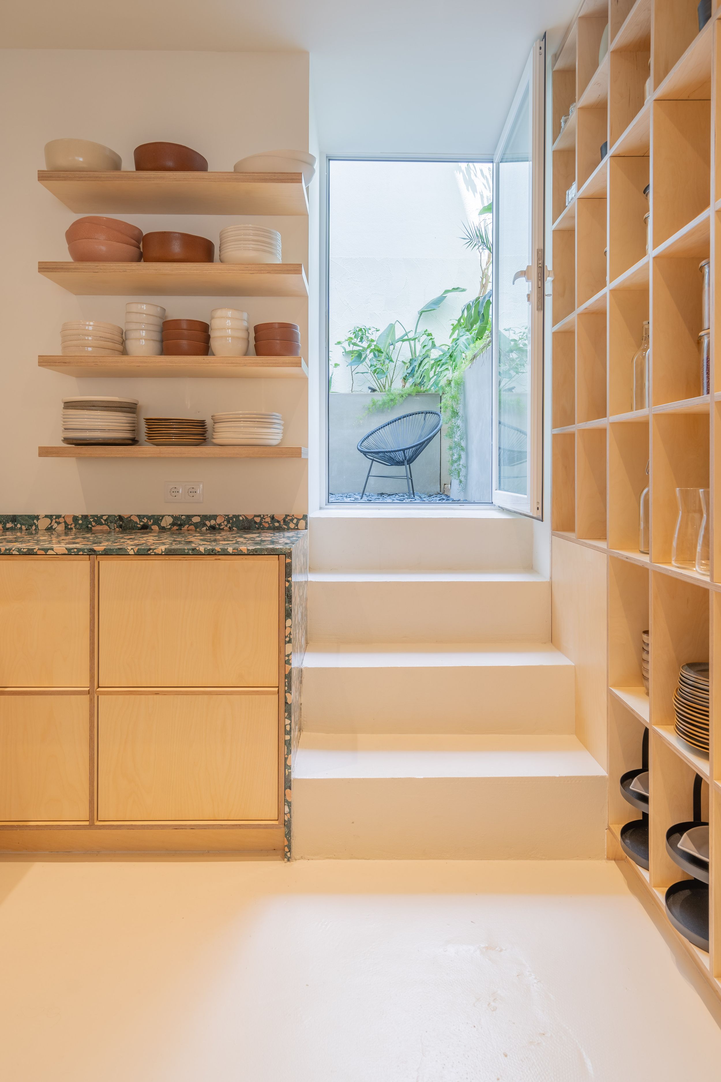 Modern storage area with wooden shelving, steps leading to window seat, and natural light.