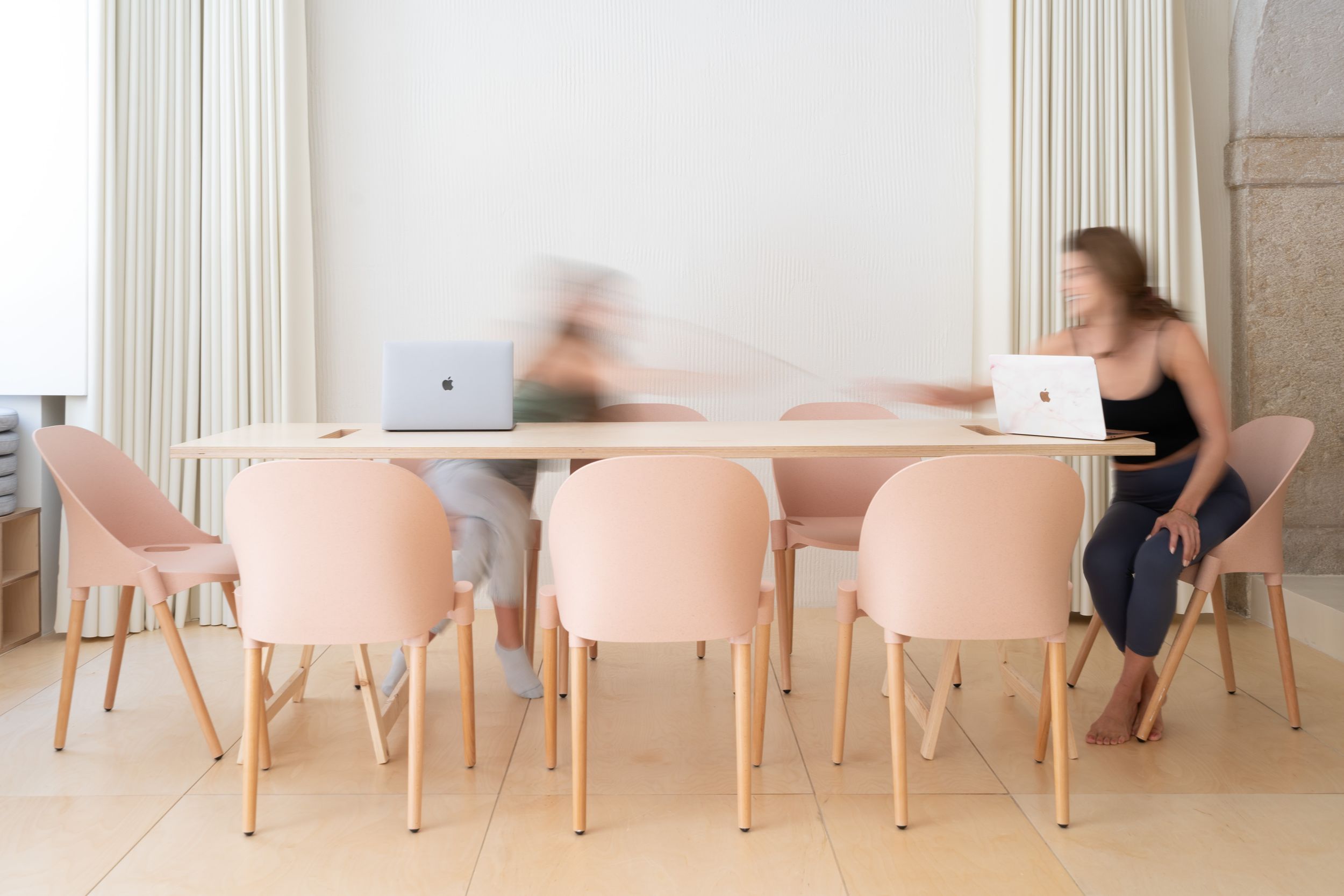 Modern dining area with soft pink chairs and wooden table in a bright, minimalist setting.