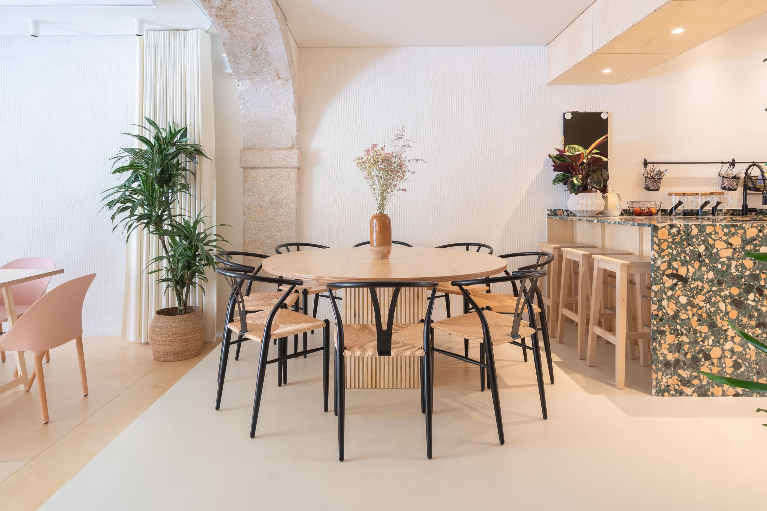 Elegant dining space with round table, black chairs, and green marble kitchen counter in background.