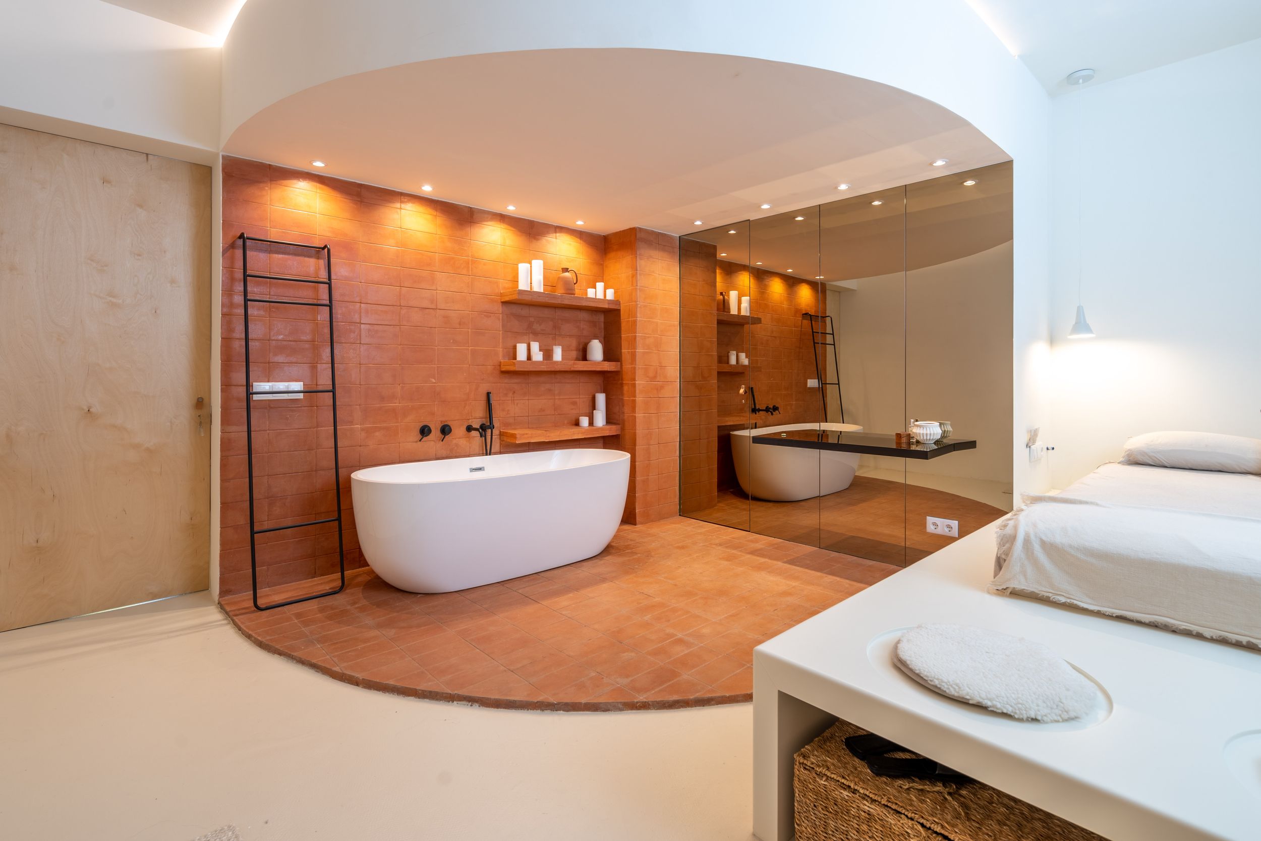 Spa-like bathroom with curved archway, freestanding tub, and warm lighting.