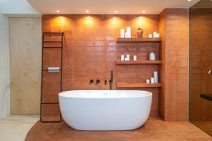 Contemporary bathroom with freestanding tub and terracotta tile walls featuring built-in shelving.