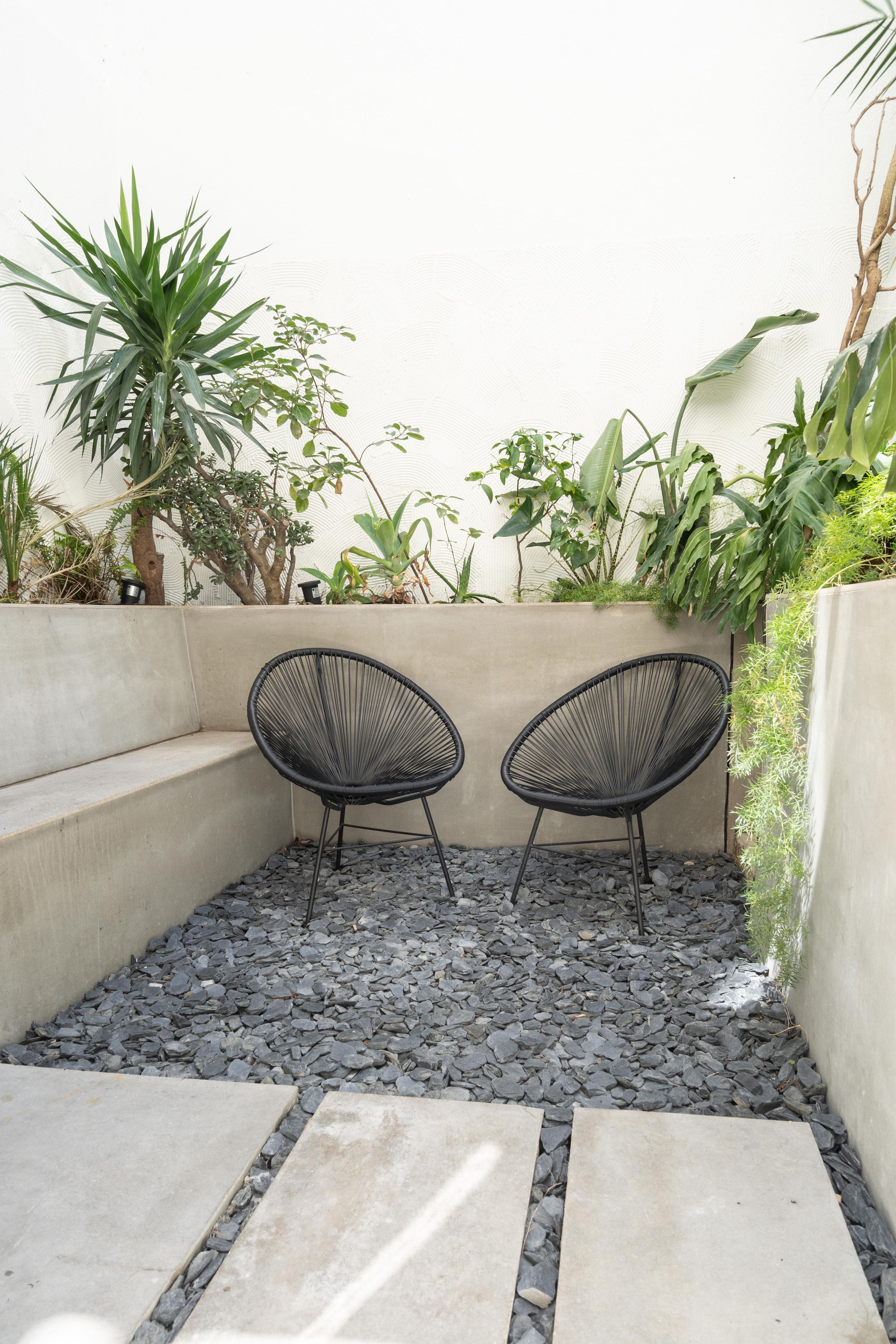 Cozy outdoor seating area with two black acapulco chairs surrounded by tropical plants and stone pavers.