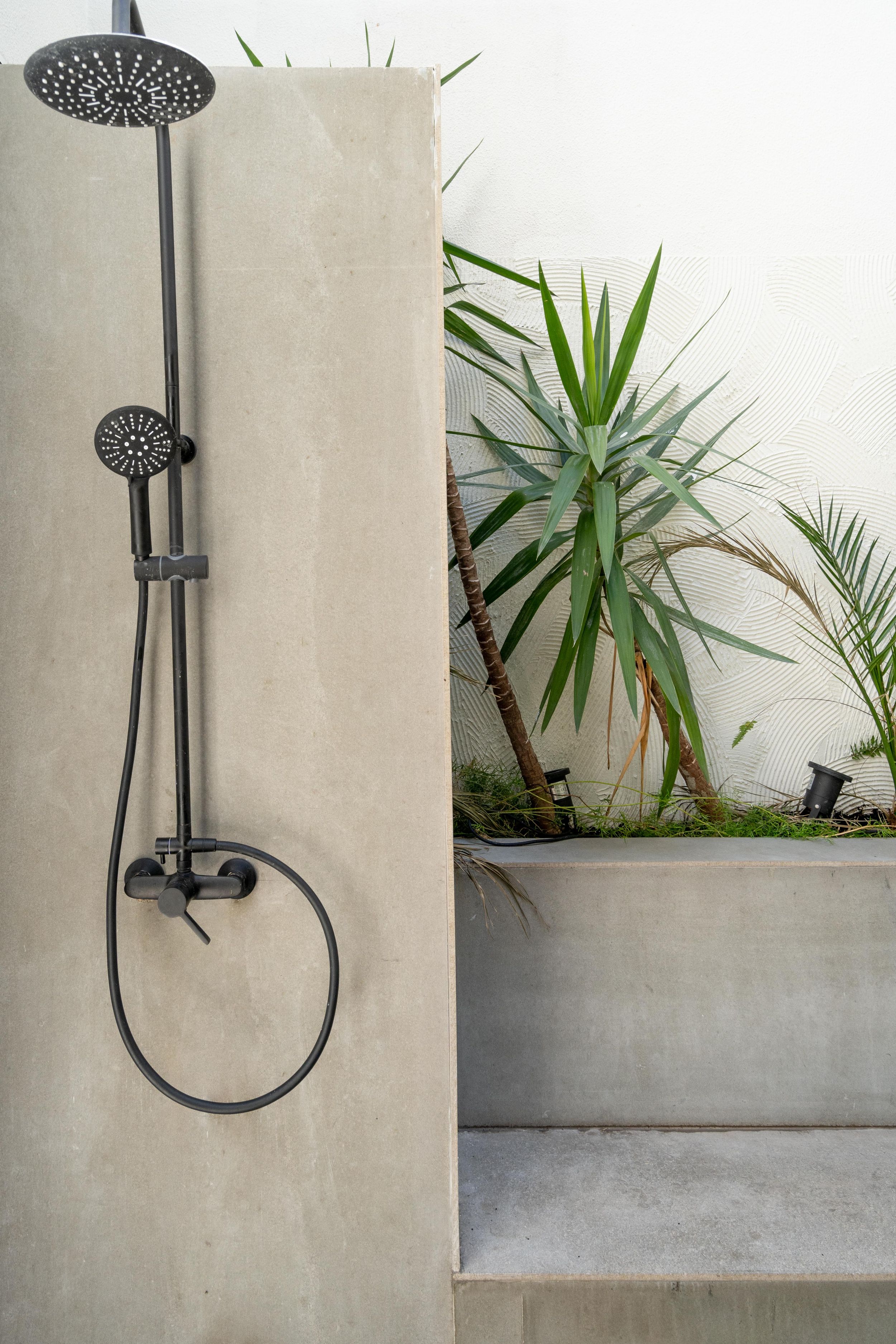Modern black rainfall shower with sliding rail system next to tropical plants in outdoor setting.