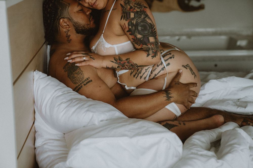 Intimate couple embrace showing tattoos in natural window light.