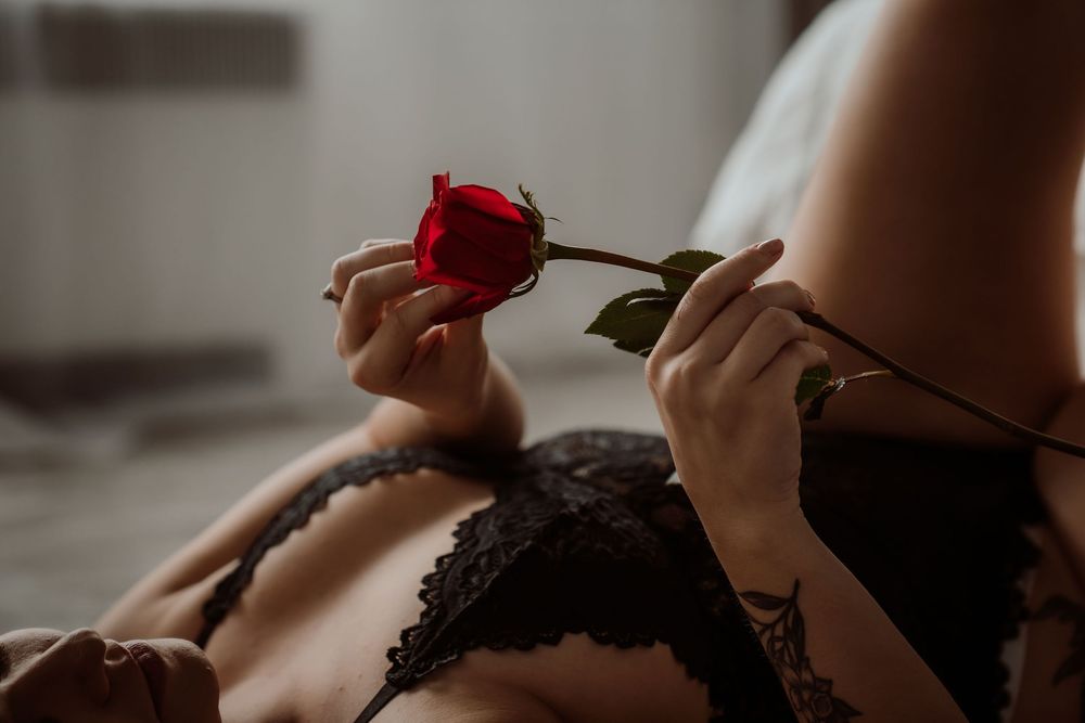 Woman in black lace lingerie holding a red rose, romantic boudoir photography with soft natural lighting.