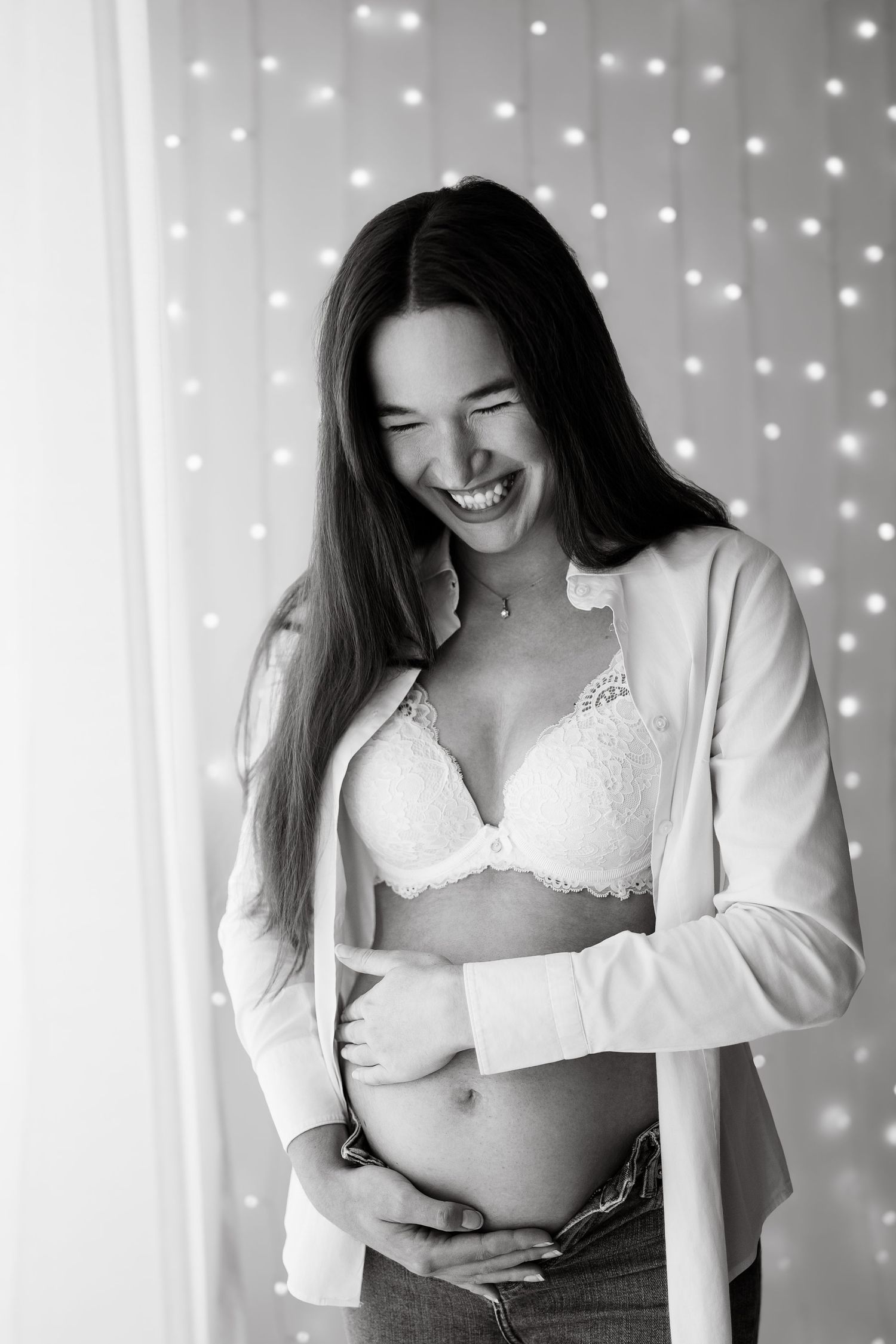 Happy pregnant woman in black and white photo laughing while holding her baby bump.