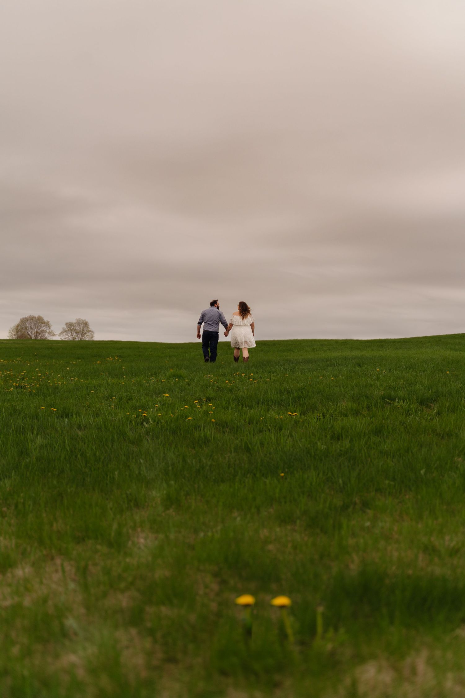 A couple sits together on a grassy hilltop under an overcast sky, creating a serene and intimate landscape scene.