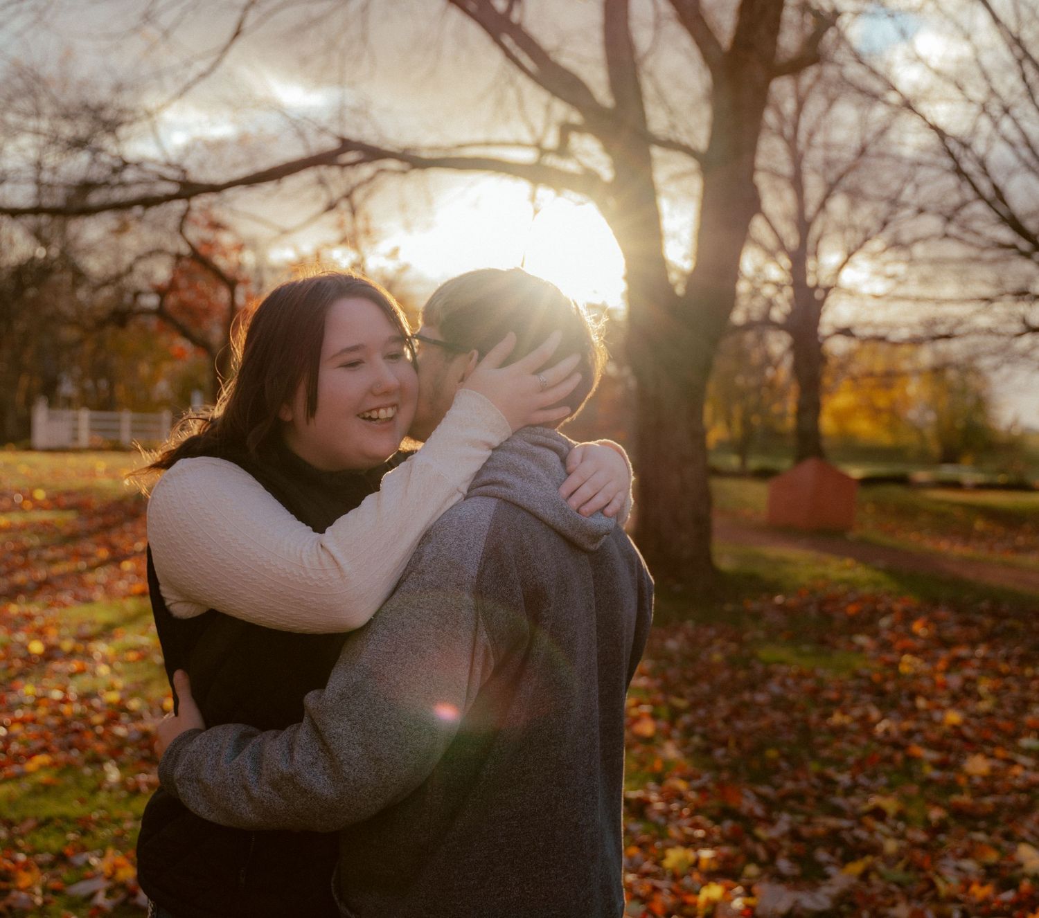 Romantic sunset embrace in park with fallen autumn leaves surrounding couple.