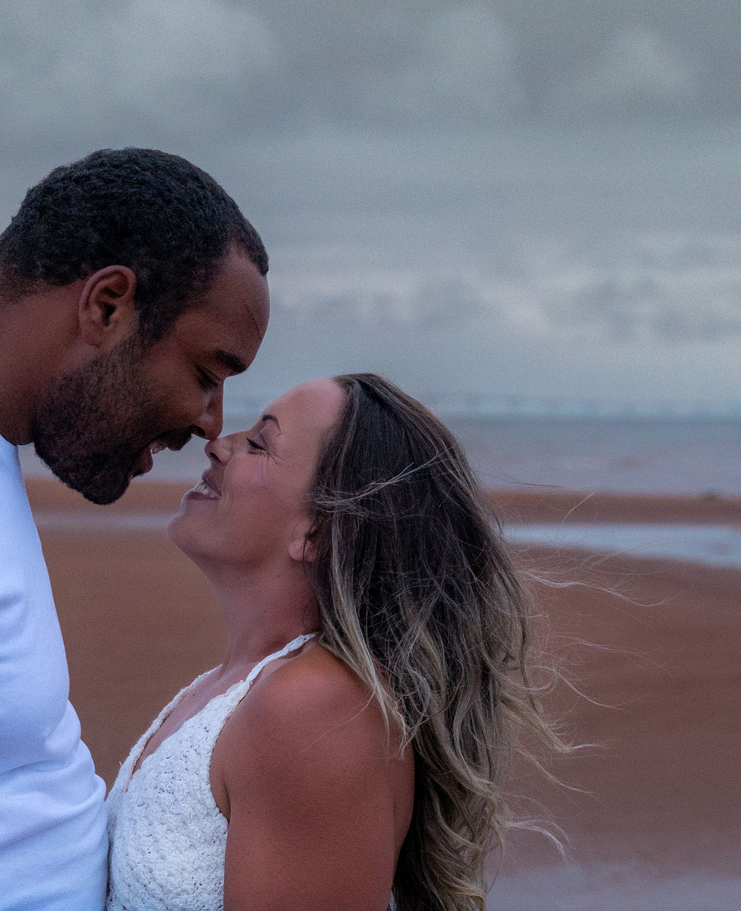 Intimate couple embracing on a cloudy beach at dusk.