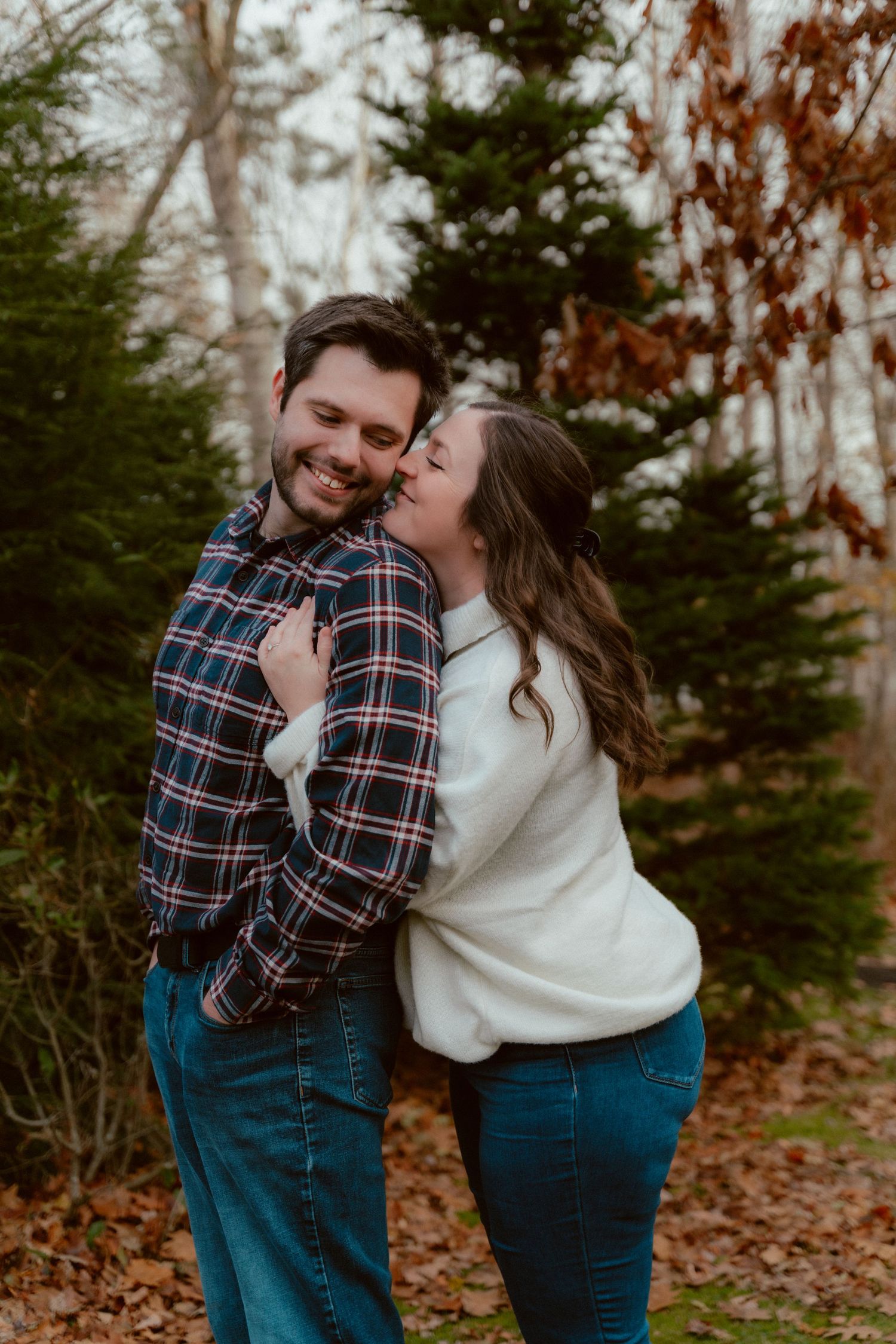 A couple in cozy fall outfits sharing a tender embrace among autumn trees.