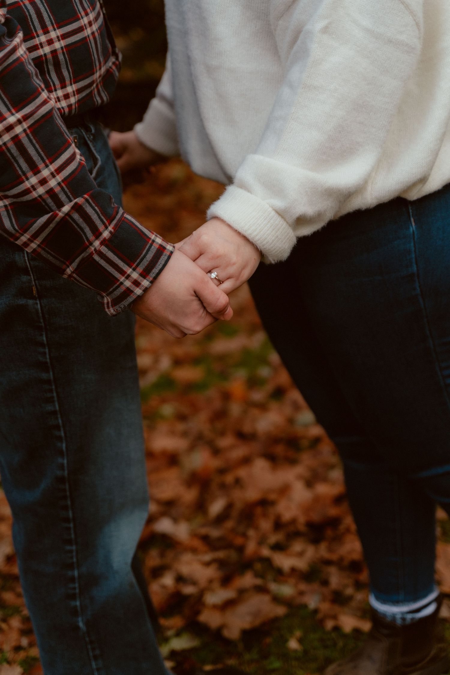 Close-up of two people holding hands while wearing casual autumn clothing.