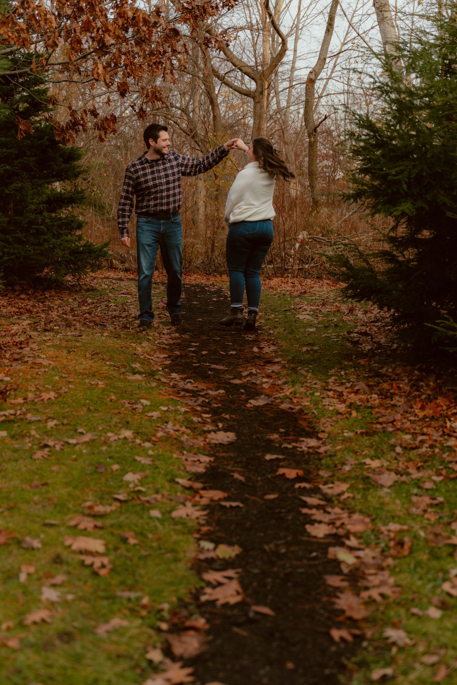 Two people dancing on a leaf-covered path surrounded by fall foliage.
