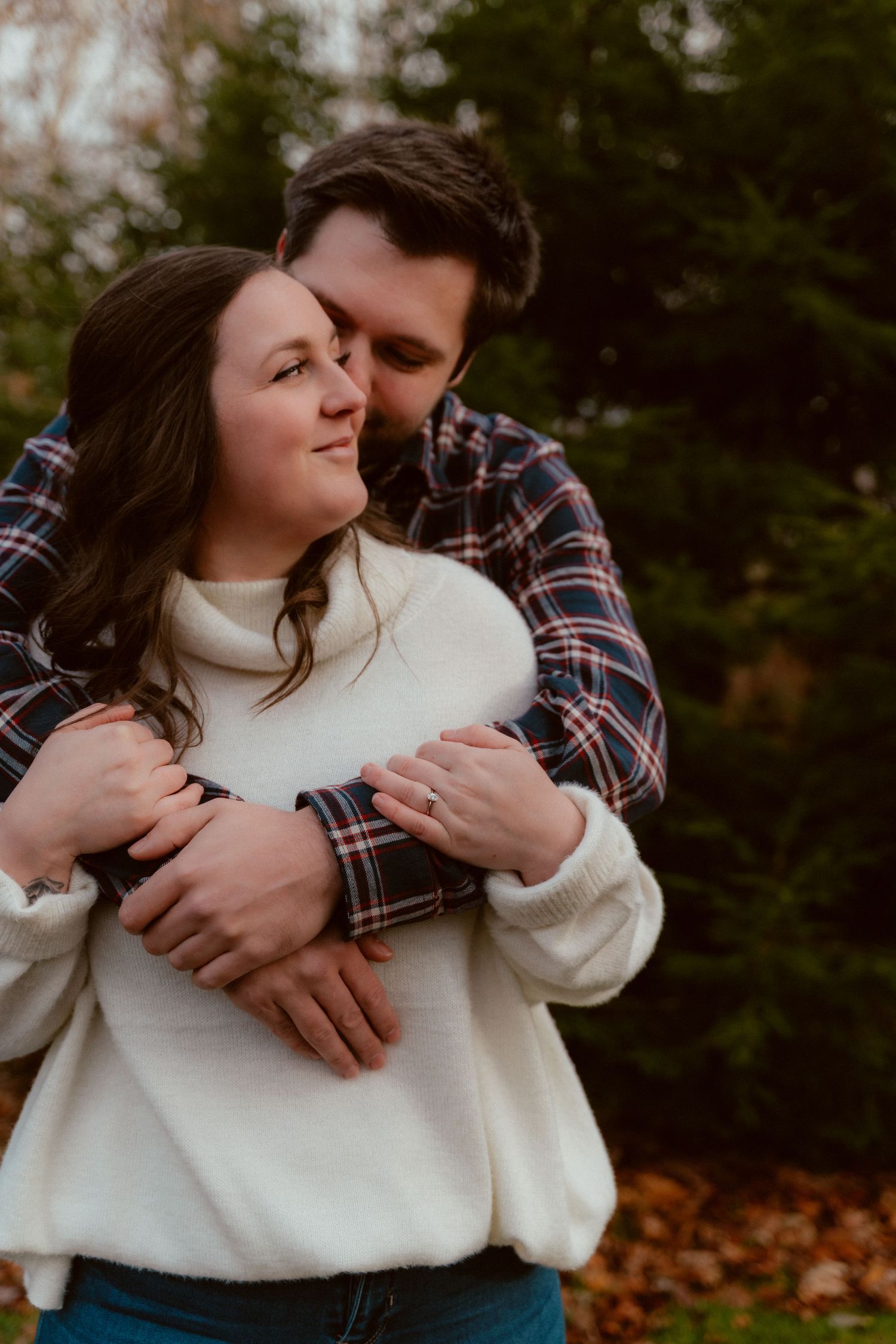 A tender embrace captured in warm autumn tones against evergreen trees.