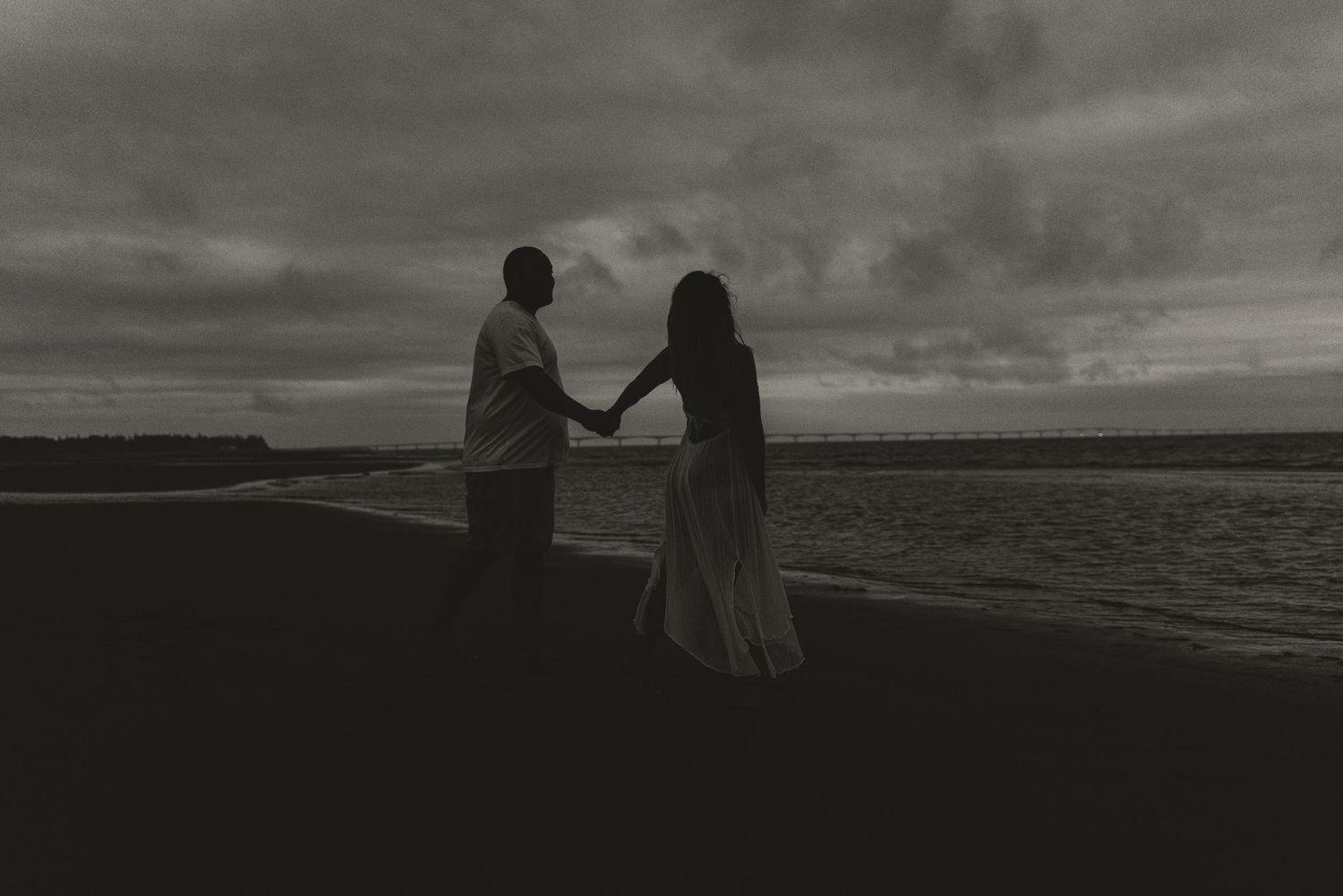 Silhouetted couple holding hands against dramatic ocean sunset.